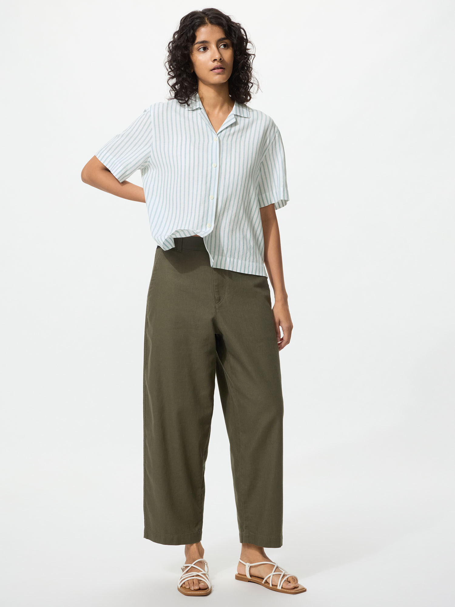 A model facing the front, wearing Linen Cotton Tapered Pants in olive-colored linen, a short sleeve blue and white striped Linen Blend Open Collar Shirt.