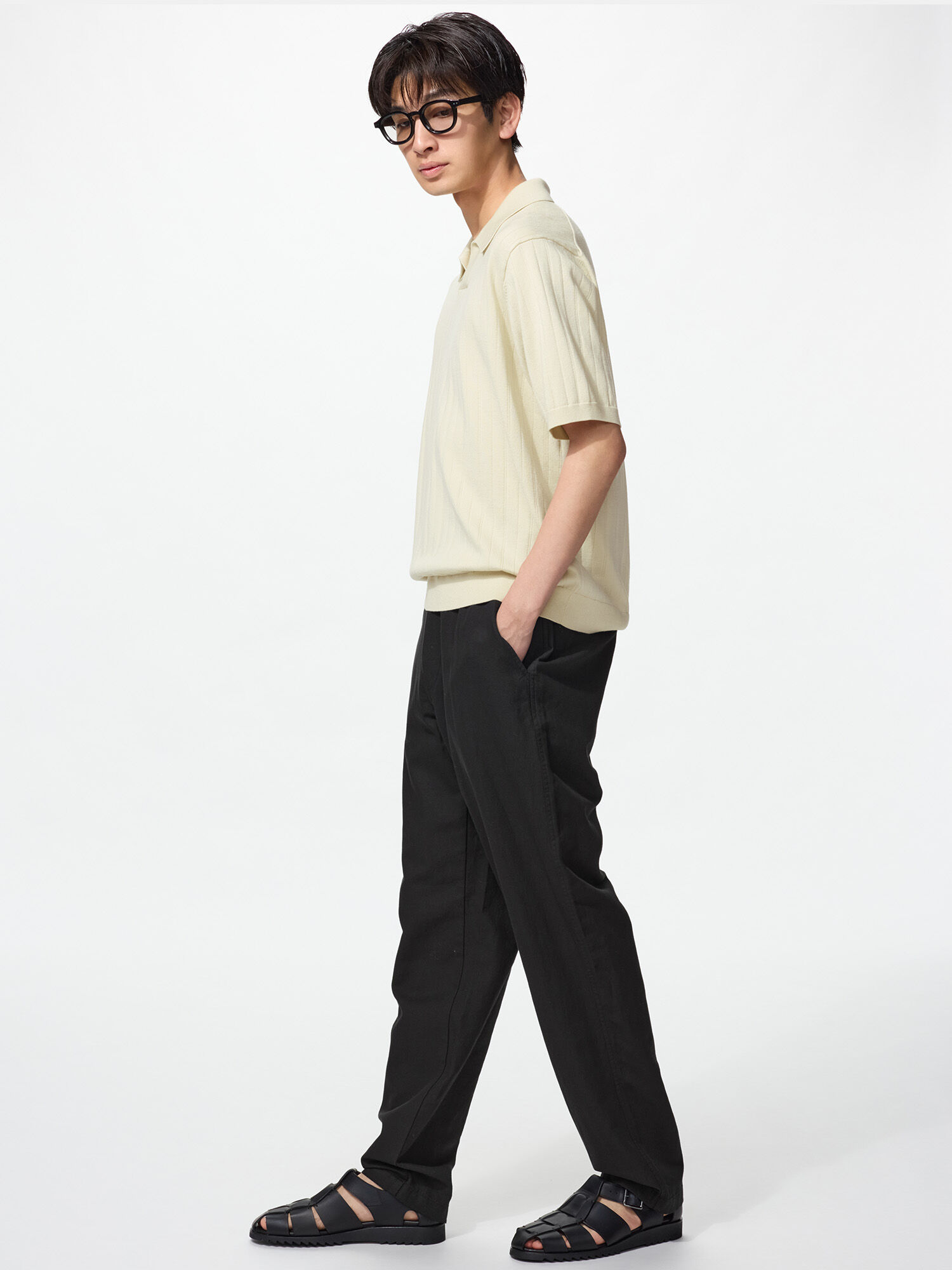 A model walking to the left. Wearing Linen Blend Relaxed Pants in black, black sandals, and a short sleeve Washable Knitted Skipper Polo Sweater in a natural beige.
