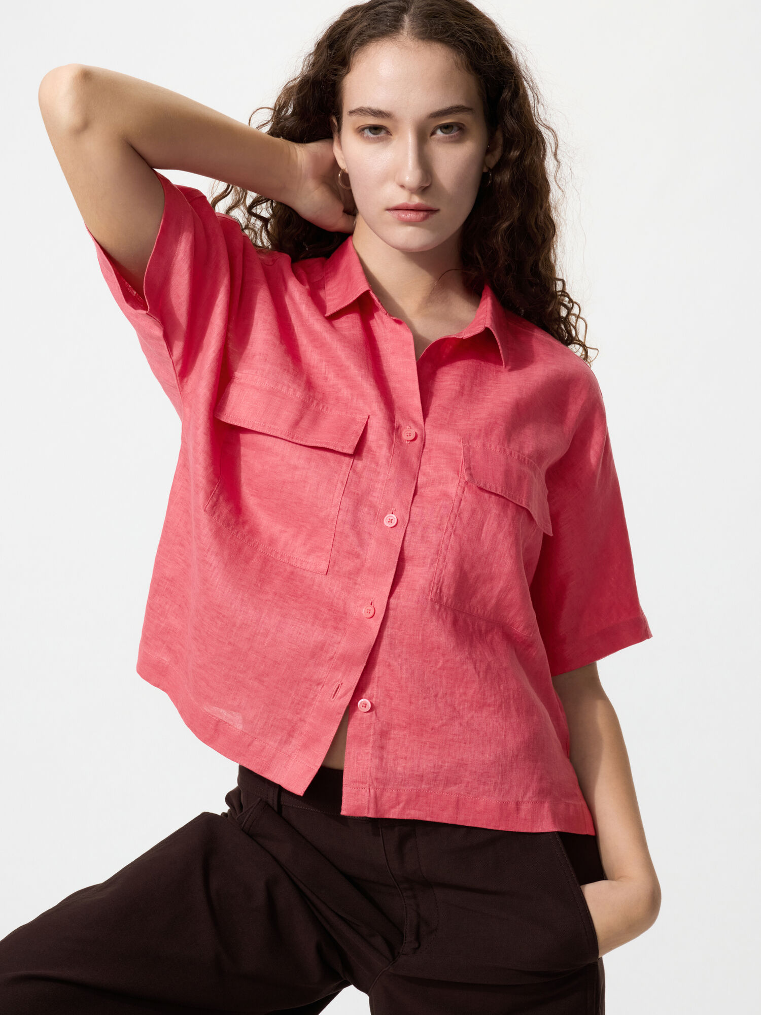 An image of a female model wearing a vibrant pink linen shirt, striking a pose with a cool expression.