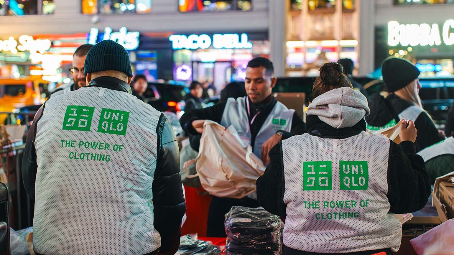 UNIQLO employees volunteer at an evening city event, sorting clothing for community distribution, supporting sustainability initiatives through The Power of Clothing.