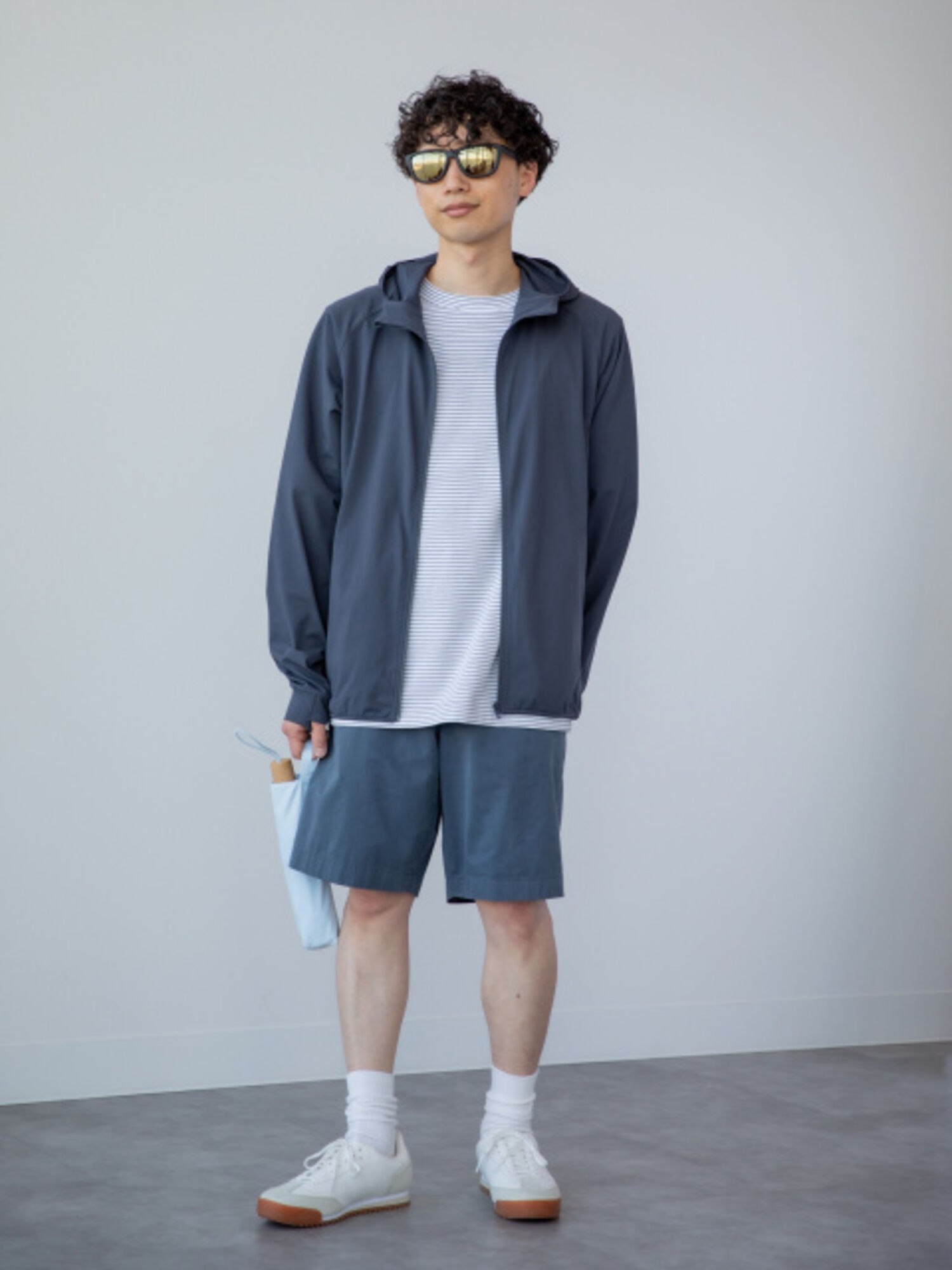 An image of a man in a full active outfit, wearing mirrored-lens sunglasses, a striped T-shirt, a navy hoodie, and a pair of shorts.